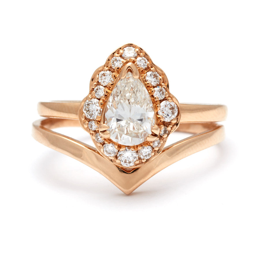 A diamond halo engagement ring with a pear white diamond center stone set in yellow gold stacked above a chevron shaped solid gold band.