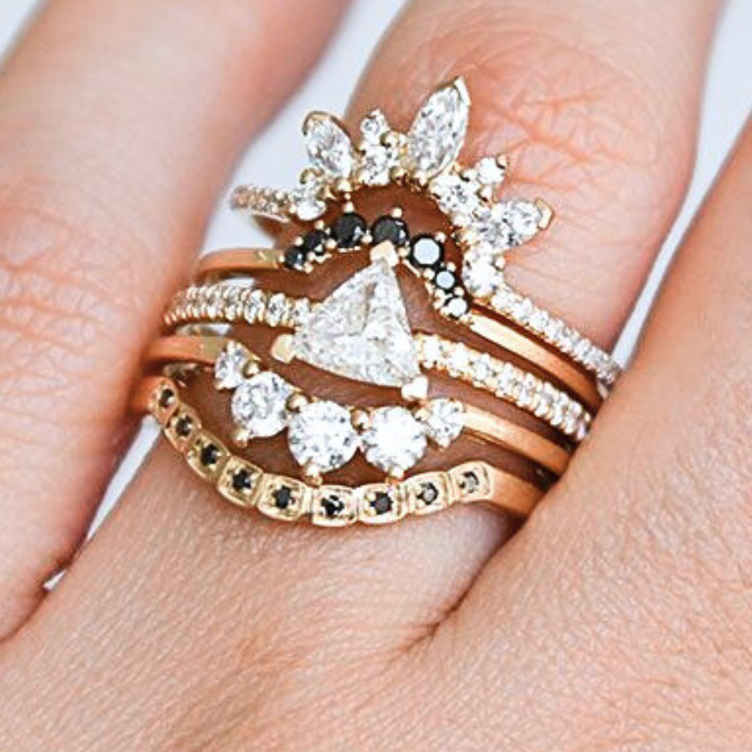 A ring stack featuring a white triangle diamond solitaire ring and nesting bands featuring an array of white and black diamonds. All set in yellow gold. 