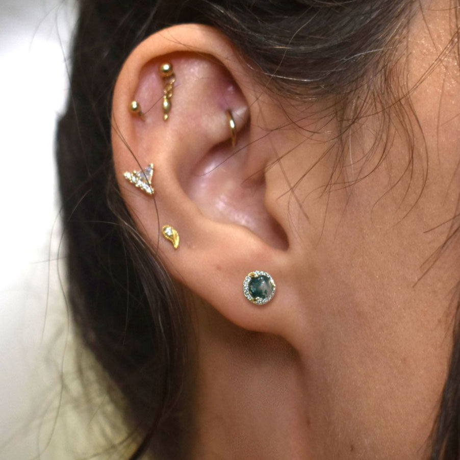 Close-up of an ear with multiple gold and silver earrings including a moss agate cabochon stud. 