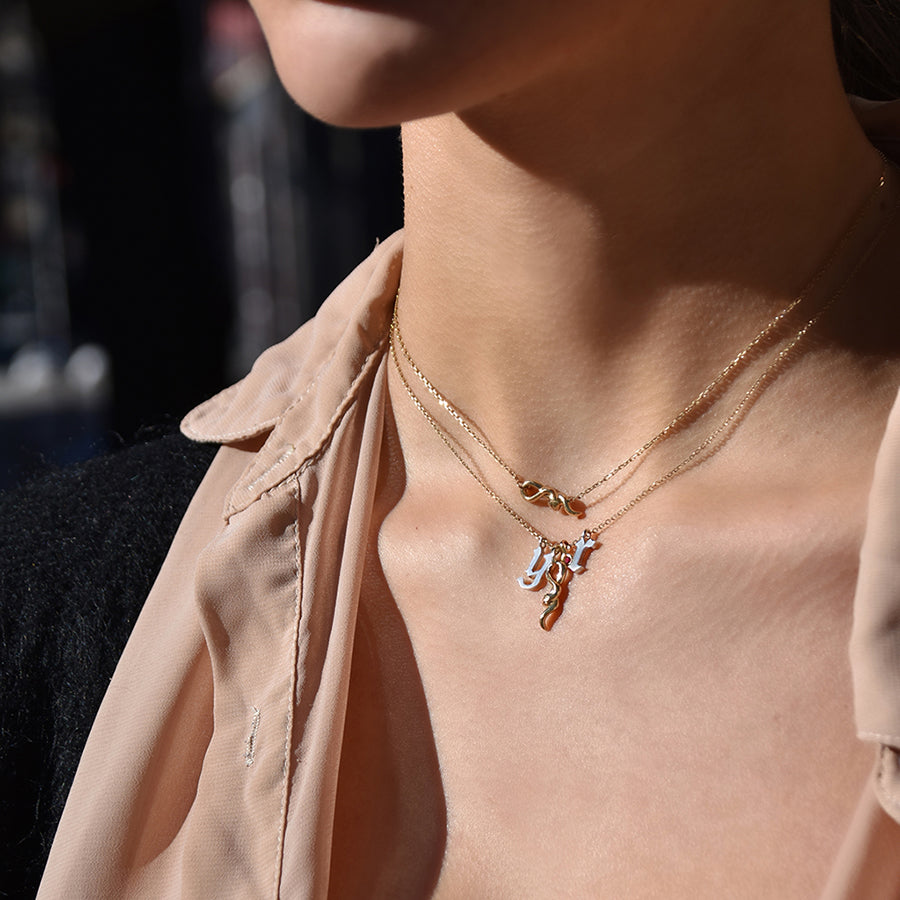 A medium sized serpent pendant set in yellow gold on a yellow gold chain with two gothic initial charms next to it with a serpent choker necklace above on a medium-complexion model's neck., White Gold, Rose Gold, Yellow Gold