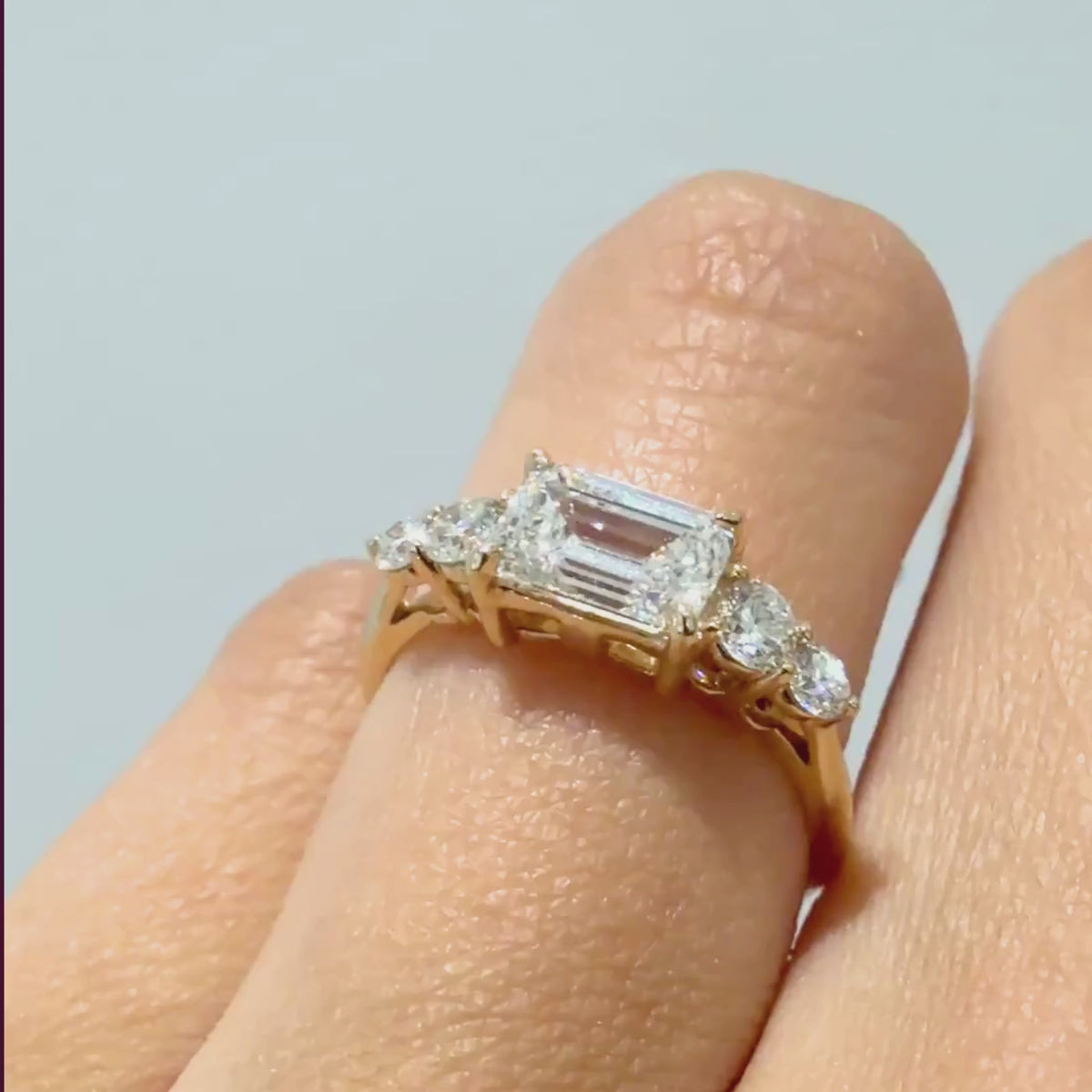 A video of a five stone white diamond engagement ring on a woman's ring finger against a grey background 