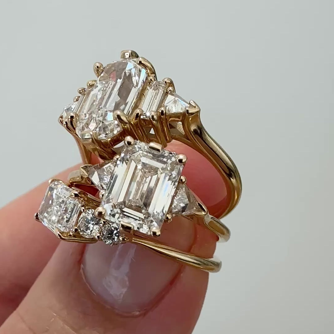 A close-up of three white diamond engagement rings in between two fingers against a white background