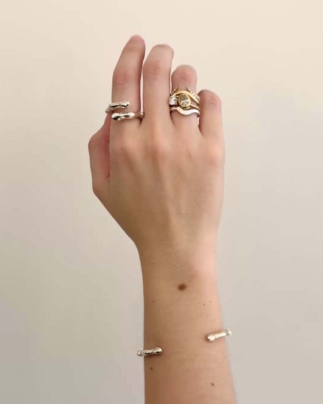 A video of a woman's hand wearing silver and diamond rings against a grey background