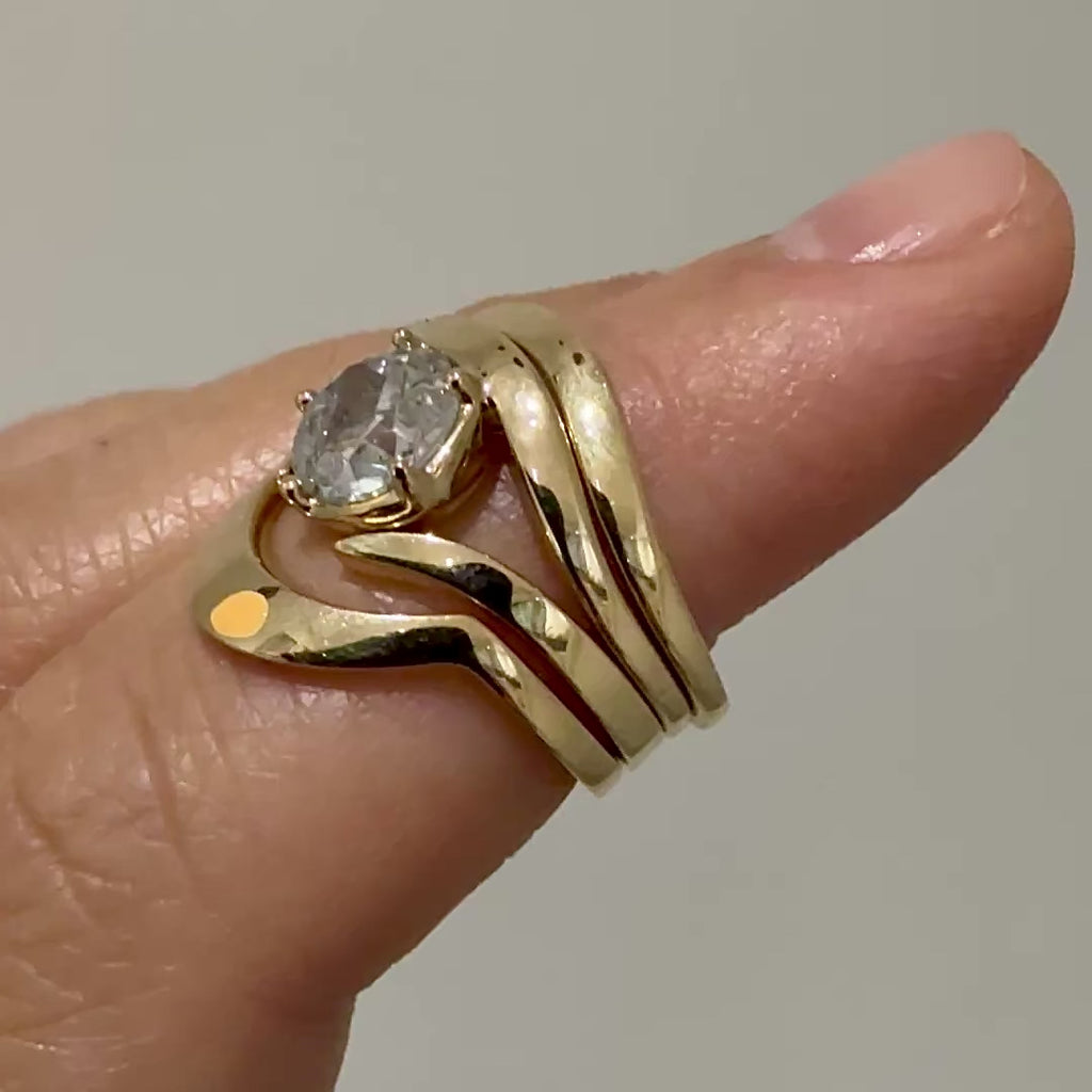 A close-up of multiple gold curved bands as well as a ring with a round grey diamond on a finger 