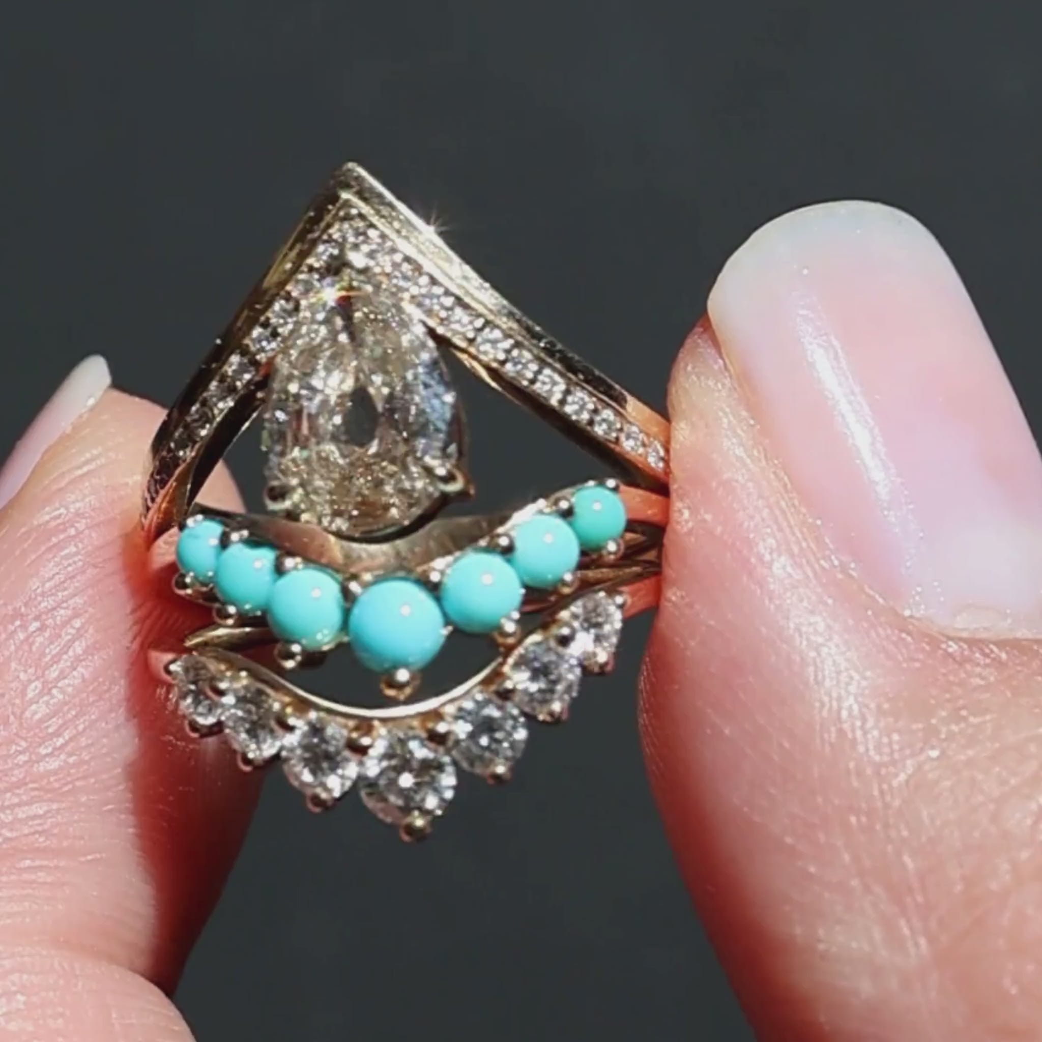 A video of three rings held in between a woman's fingers sparkling in the sunlight against a black background. The rings feature one pear cut champagne diamond yellow gold engagemnet ring, a turquoise cabochon yellow gold curved band, and a white diamond yellow gold curved band.