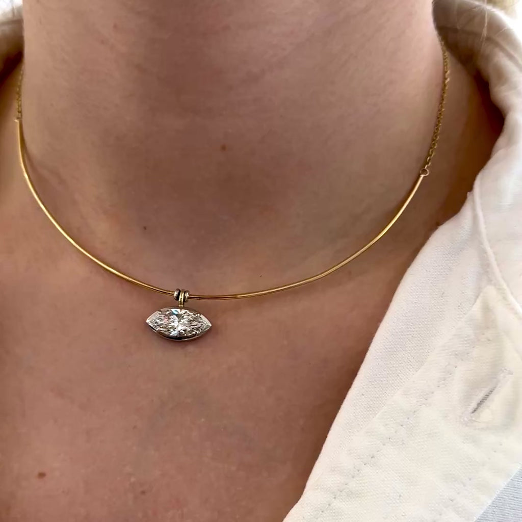 A video of a necklace with a diamond pendant on a person wearing a beige top.