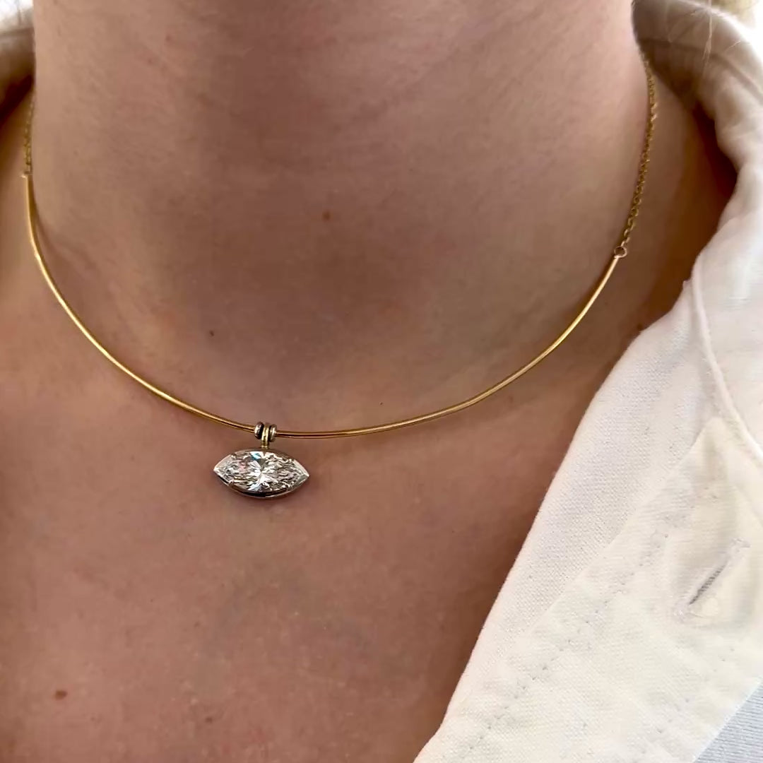 A video of a necklace with a diamond pendant on a person wearing a beige top.