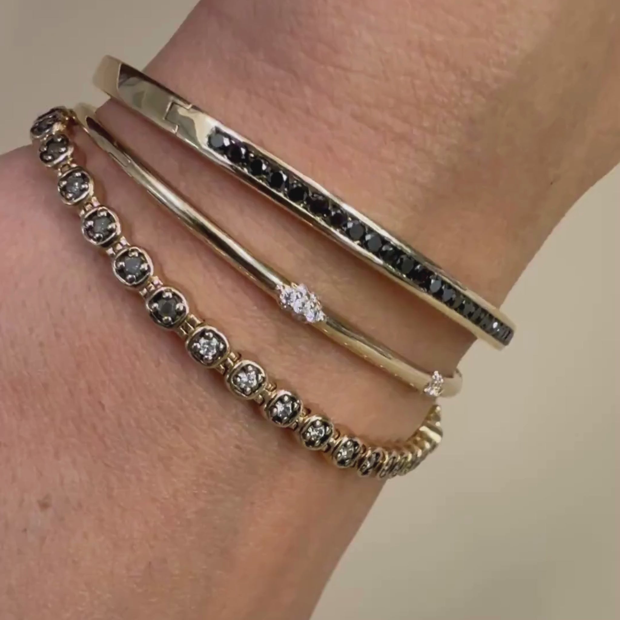 A video highlighting three gold diamond bracelets on a wrist against a beige background