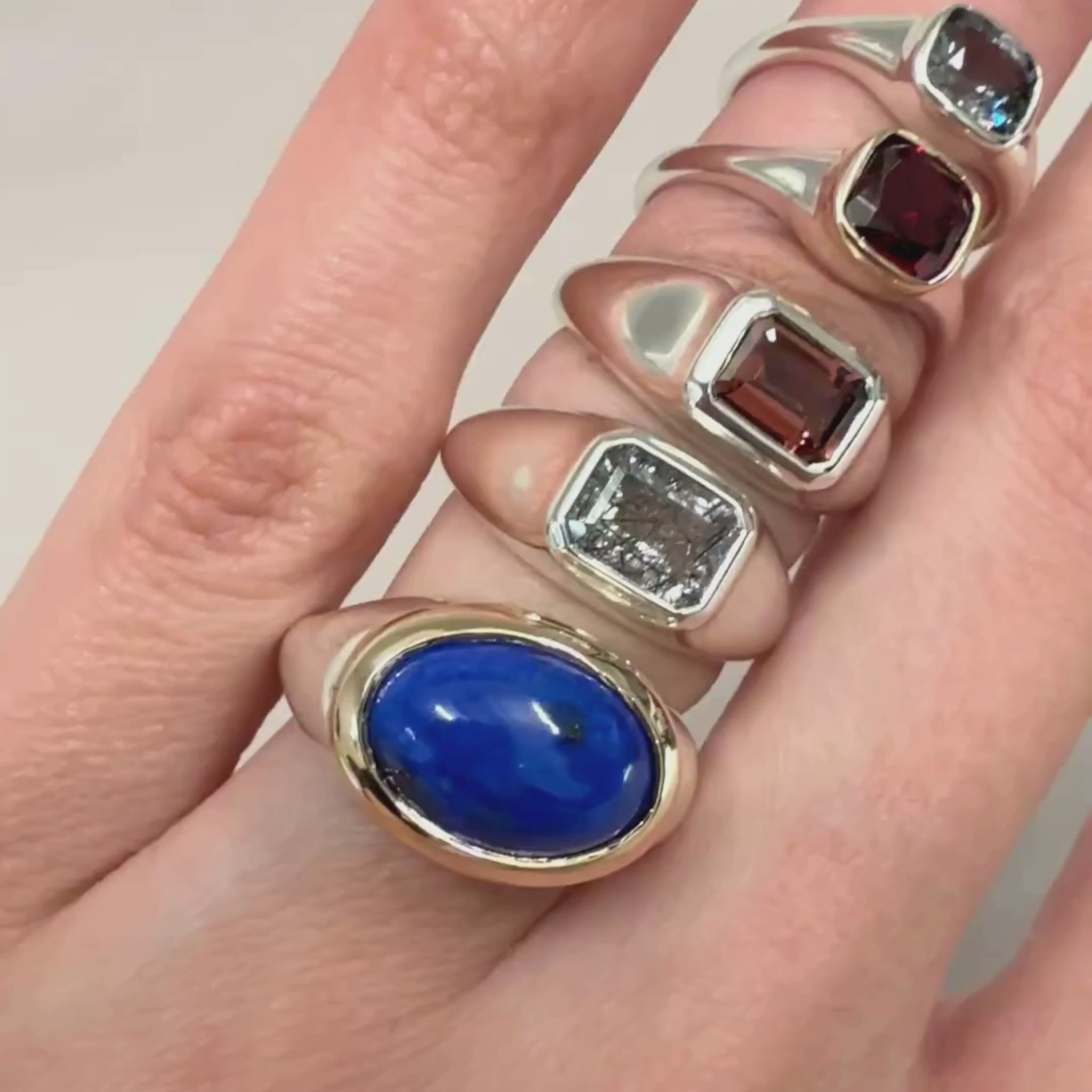 A video of a hand with multiple sterling silver gemstone rings on a grey background 