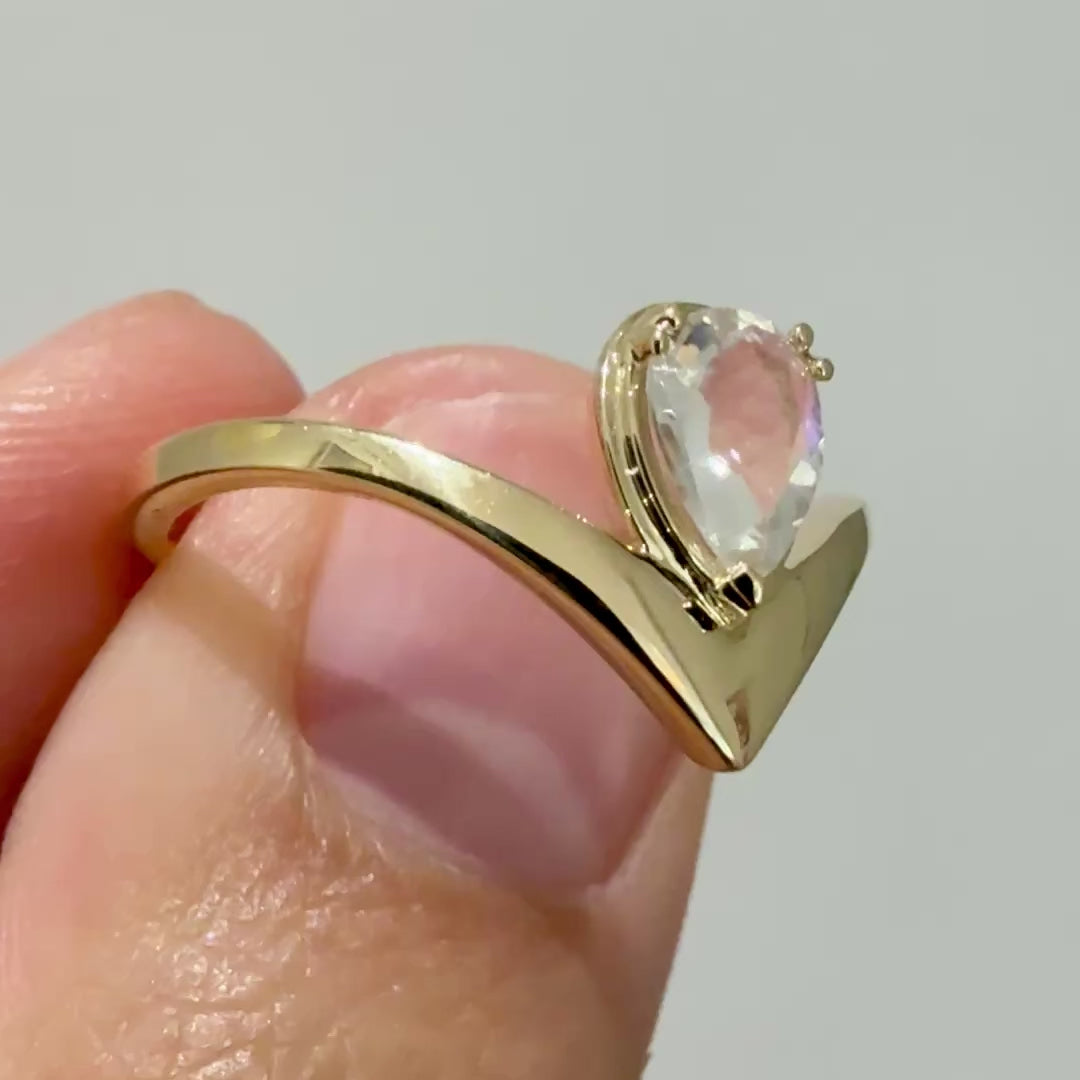 A video of a yellow gold v-shaped ring with a pear shaped rainbow moonstone between two fingers 