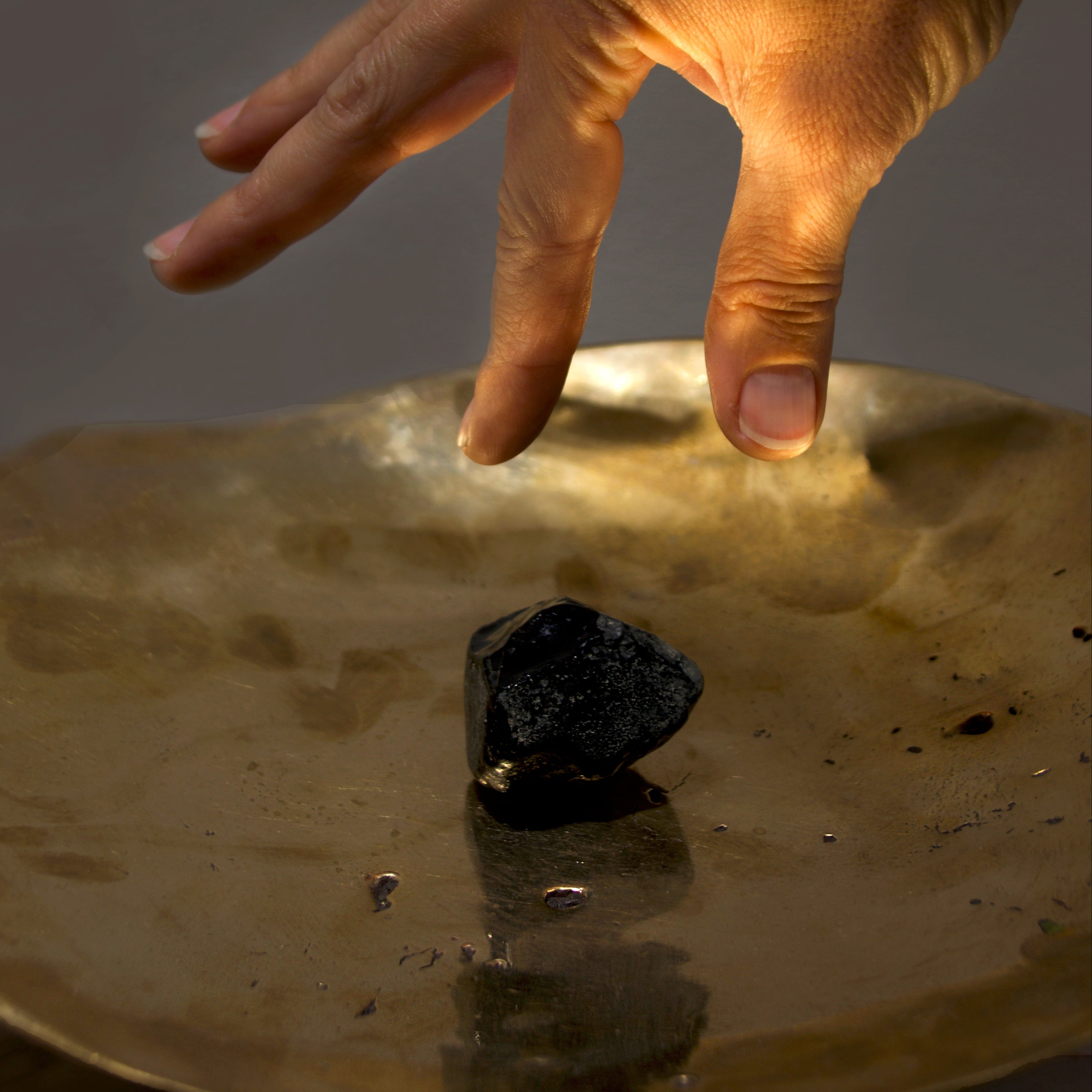 Hand reaching towards a black object on a reflective gold surface with a dark background