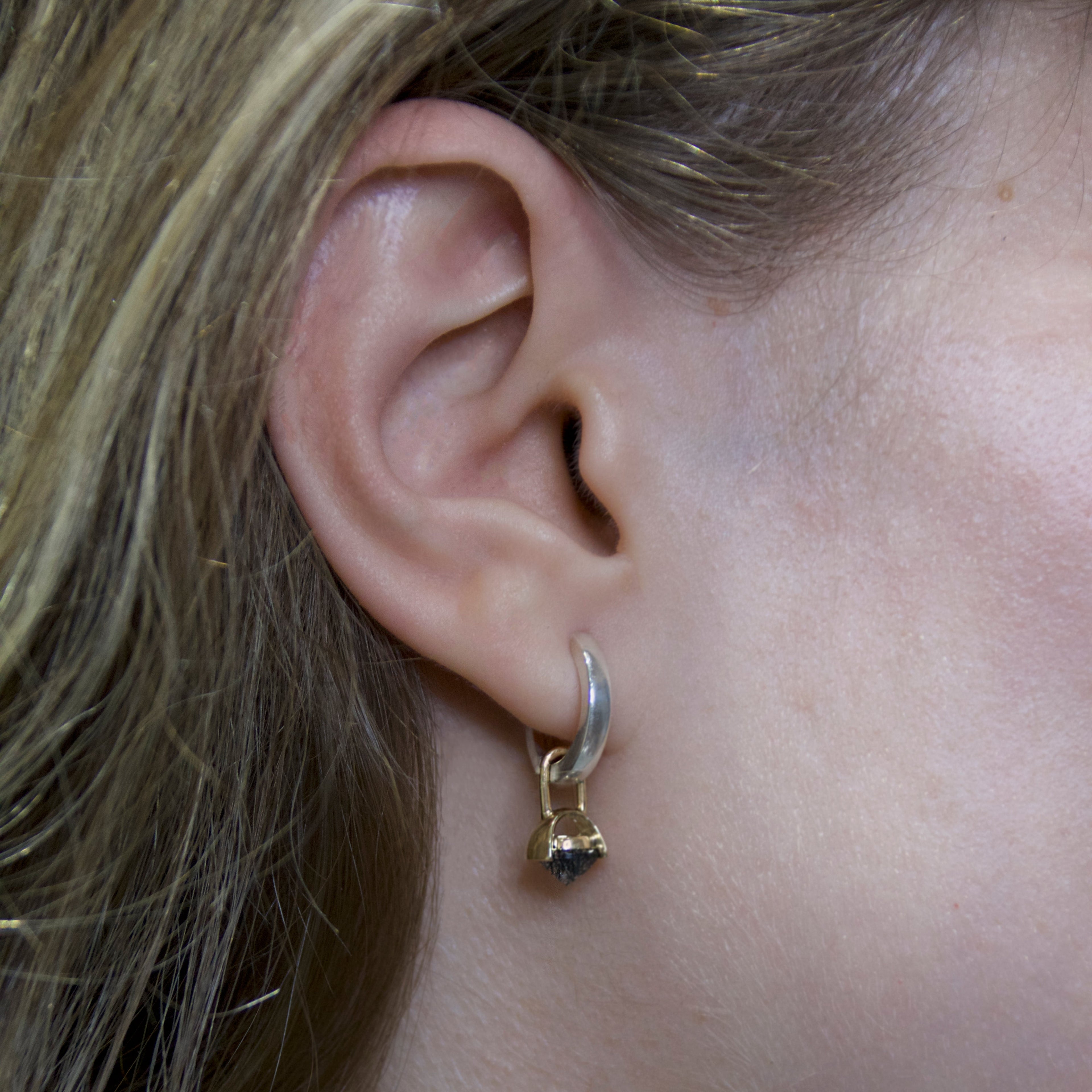 A picture of a silver hoop earring with a gold drop detail and inverted black rutile quartz gemstone on a woman's ear. 
