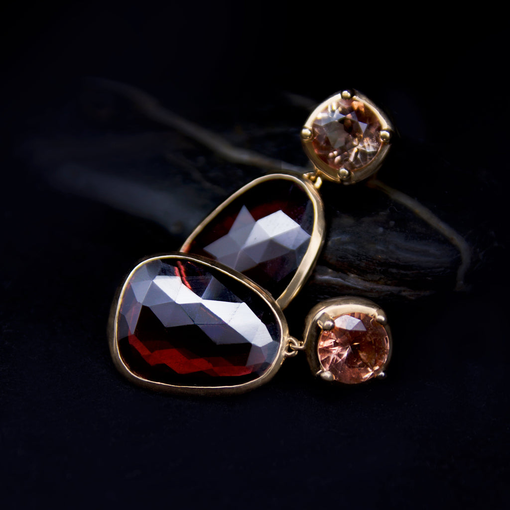 Pair of gold earrings with brownish gold susntones and pink tourmaline gemstones on a dark background
