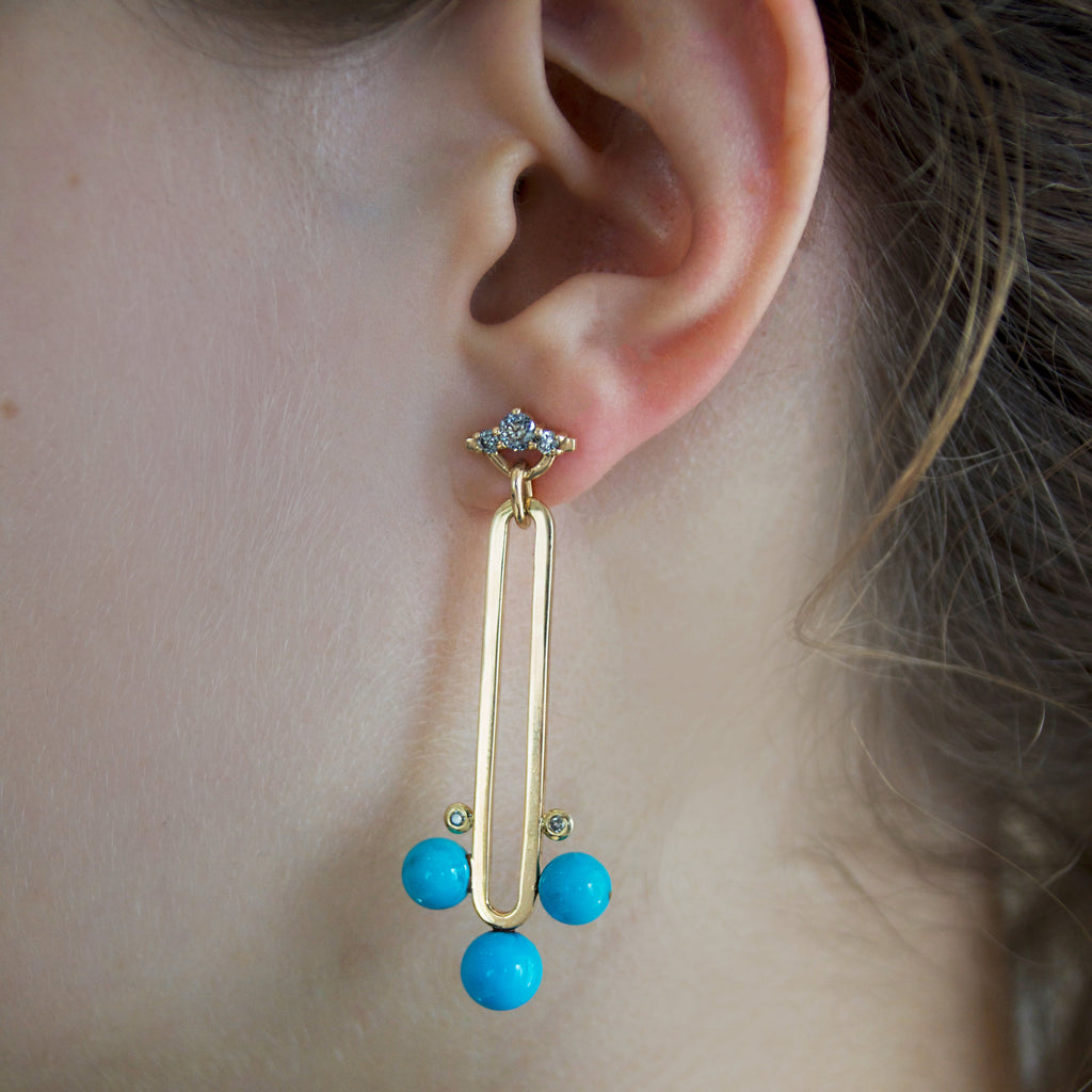 Gold drop earring with grey diamonds and blue turquoise beads worn by a person