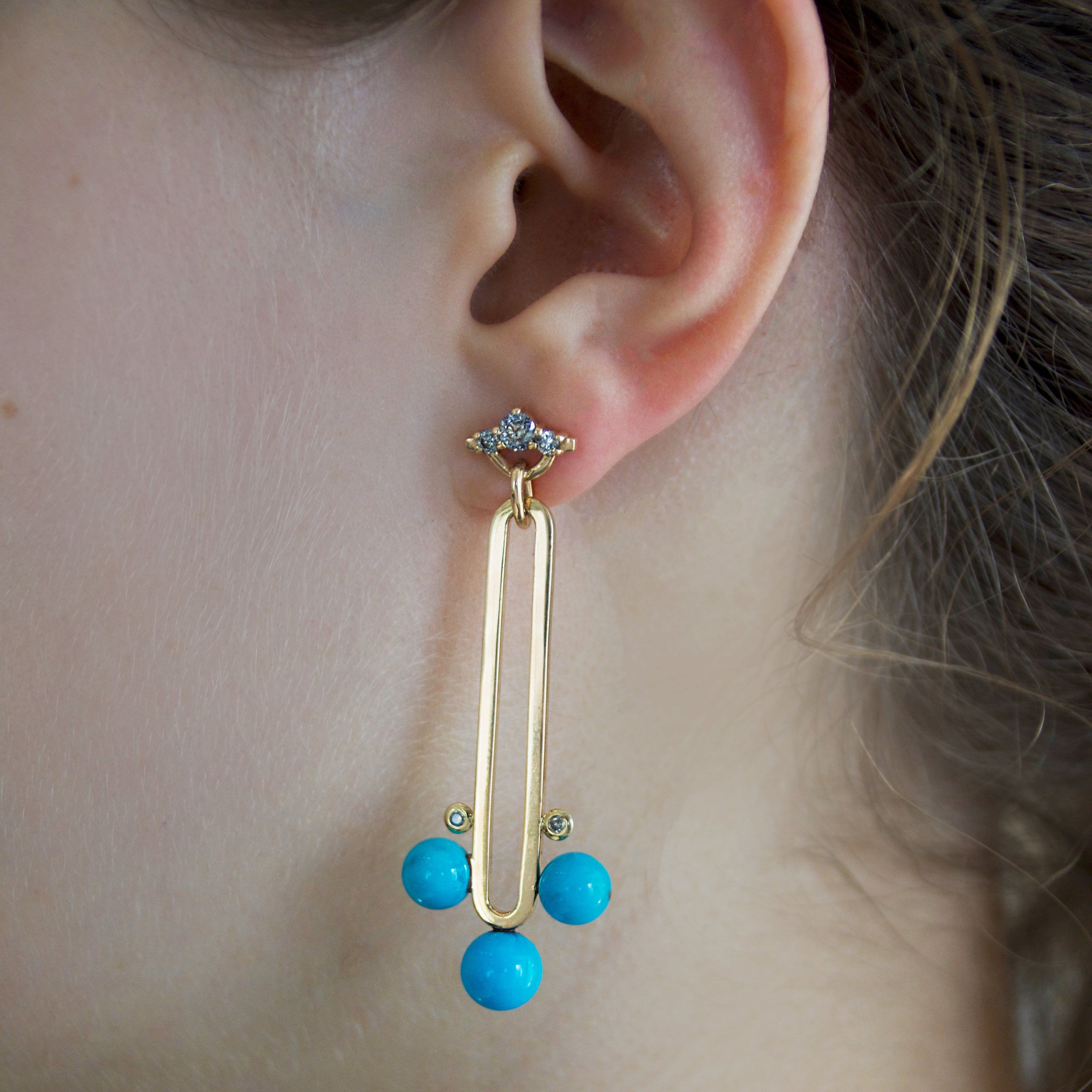 Gold drop earring with grey diamonds and blue turquoise beads worn by a person