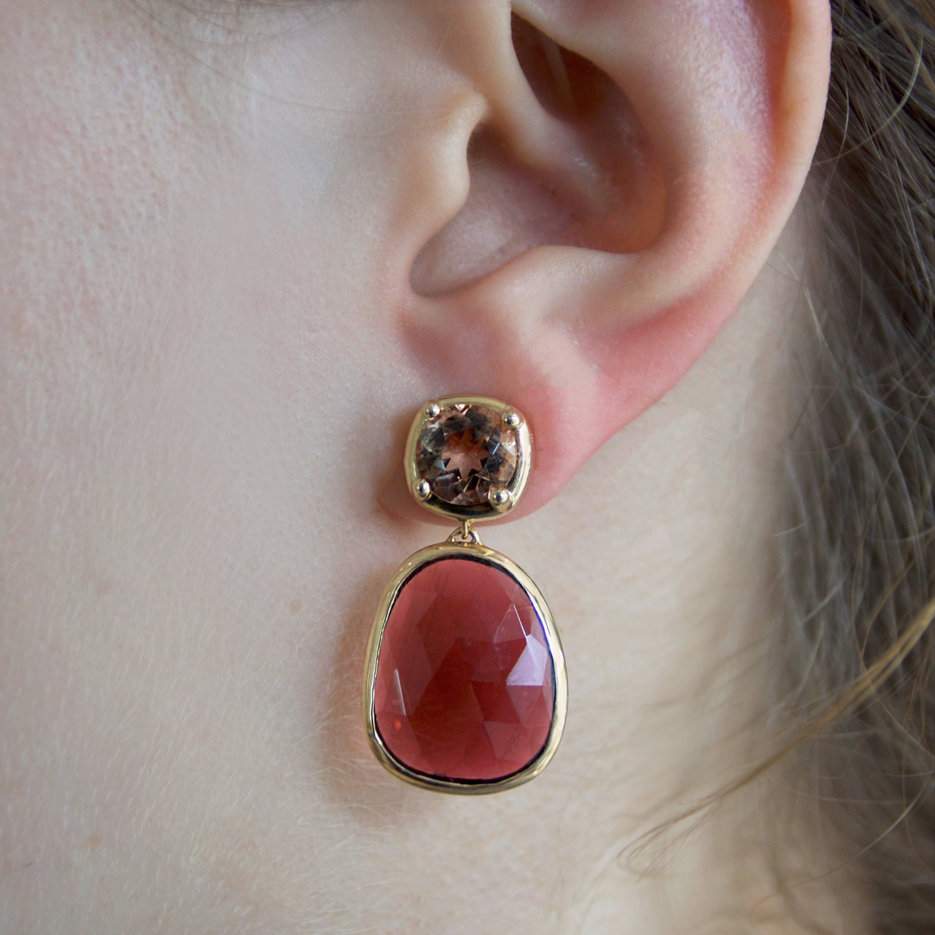 Close-up of an ear wearing a pink tourmaline stone earring with brownish-gold sunstones set in yellow gold.