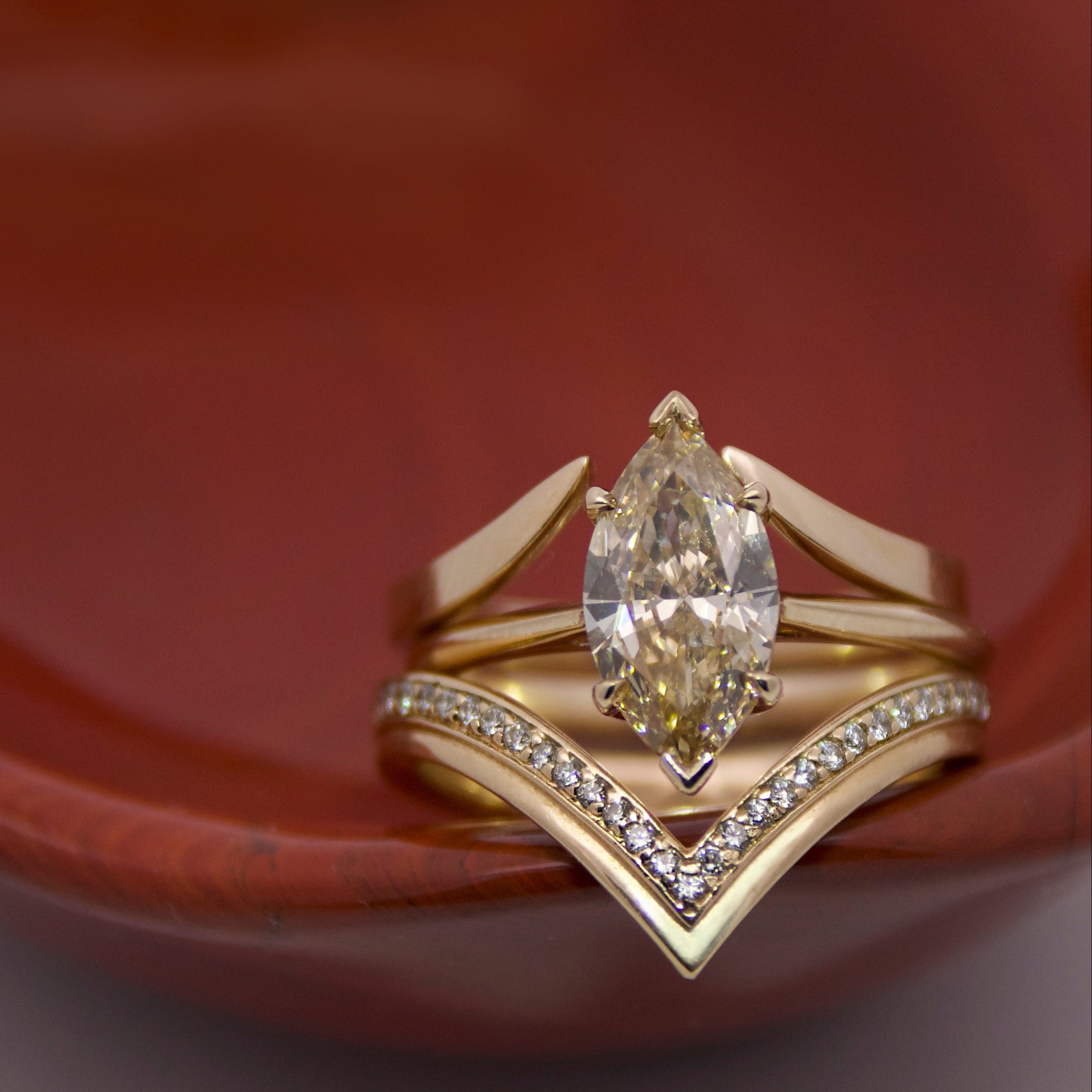 Gold ring with a marquise champagne  diamond and two gold nesting bands in a red bowl 