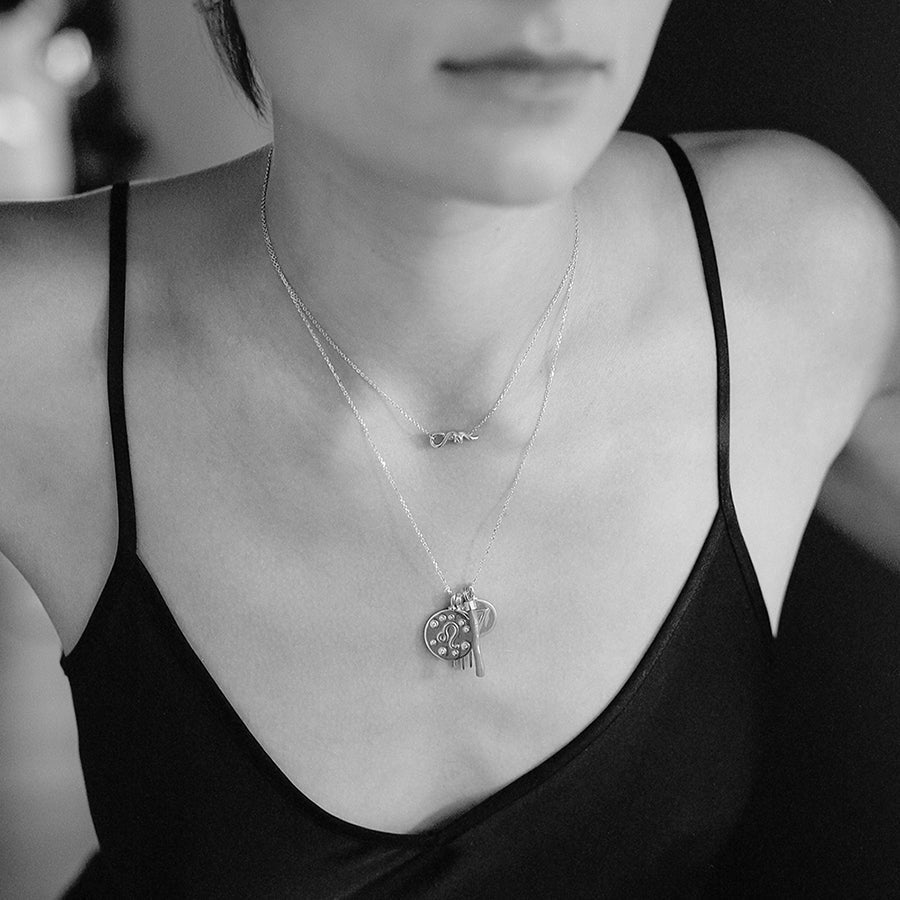 A black and white image of a model with a serpent choker necklace stacked above a zodiac charm necklace with initial charm accents.