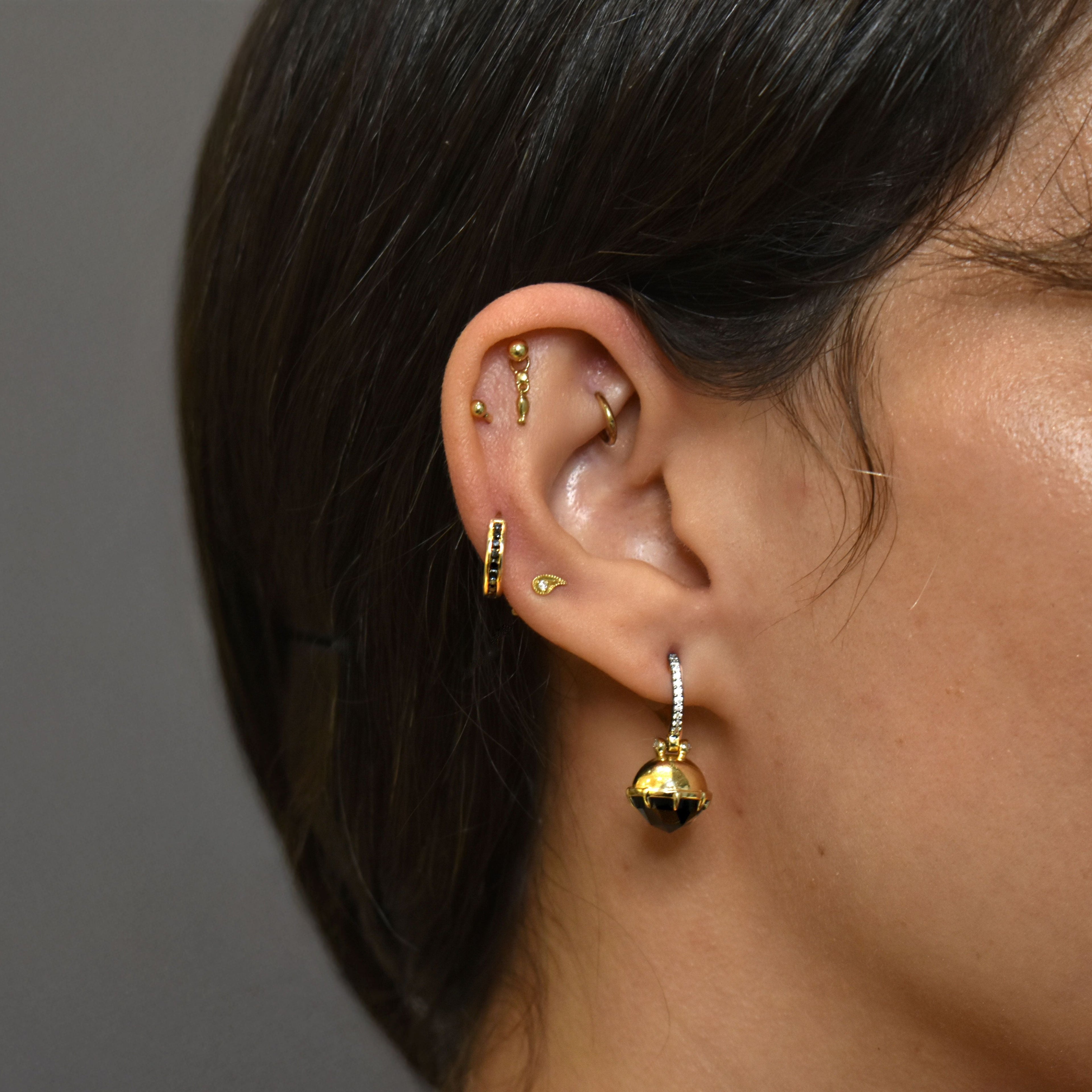 A photo of an ear with multiple gold earrings including a black spinel drop earring with diamond pave.