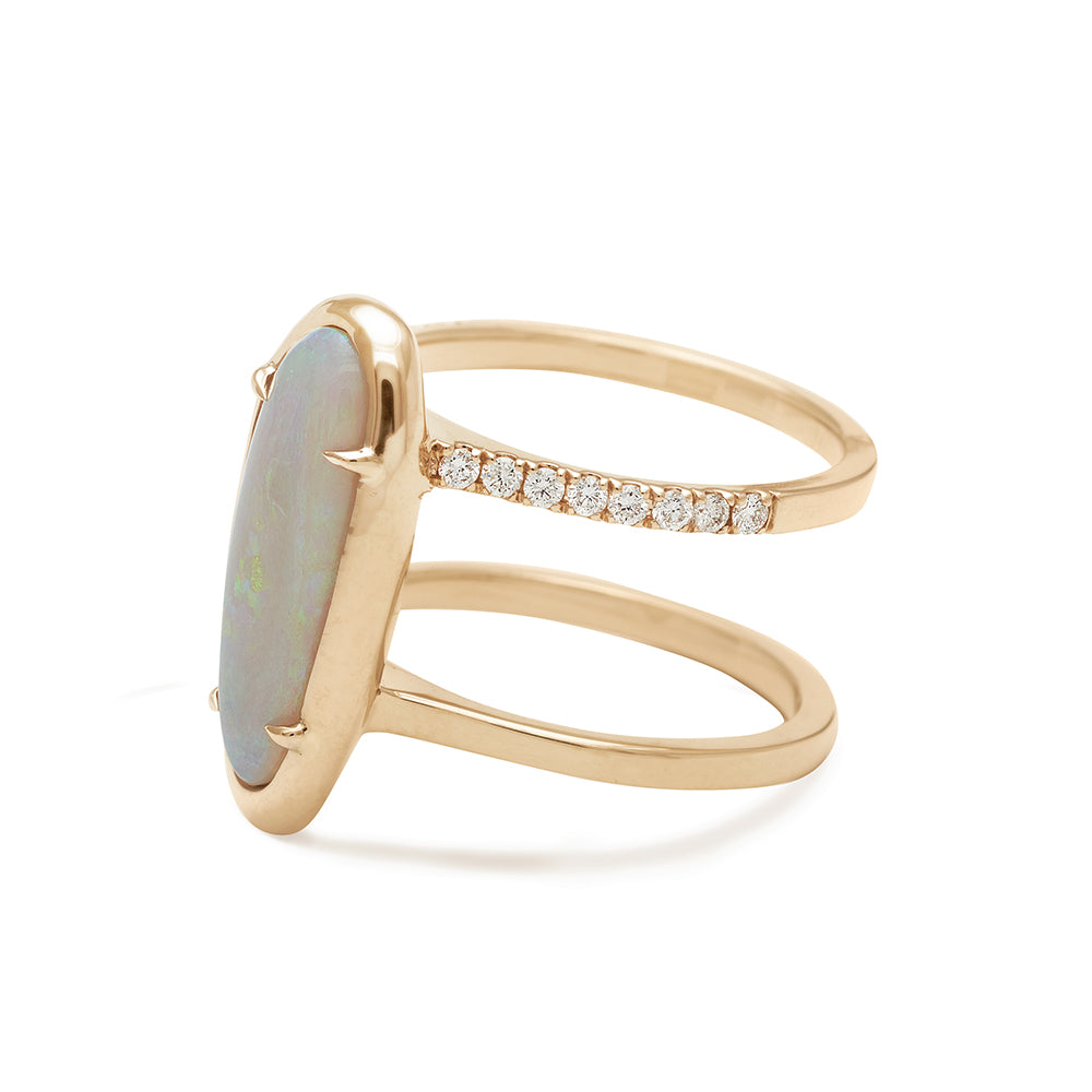 Angled view of a double banded engagement ring with white diamond pave around one of the bands in the center an oval opal stone set in yellow gold bezel with claw prongs.