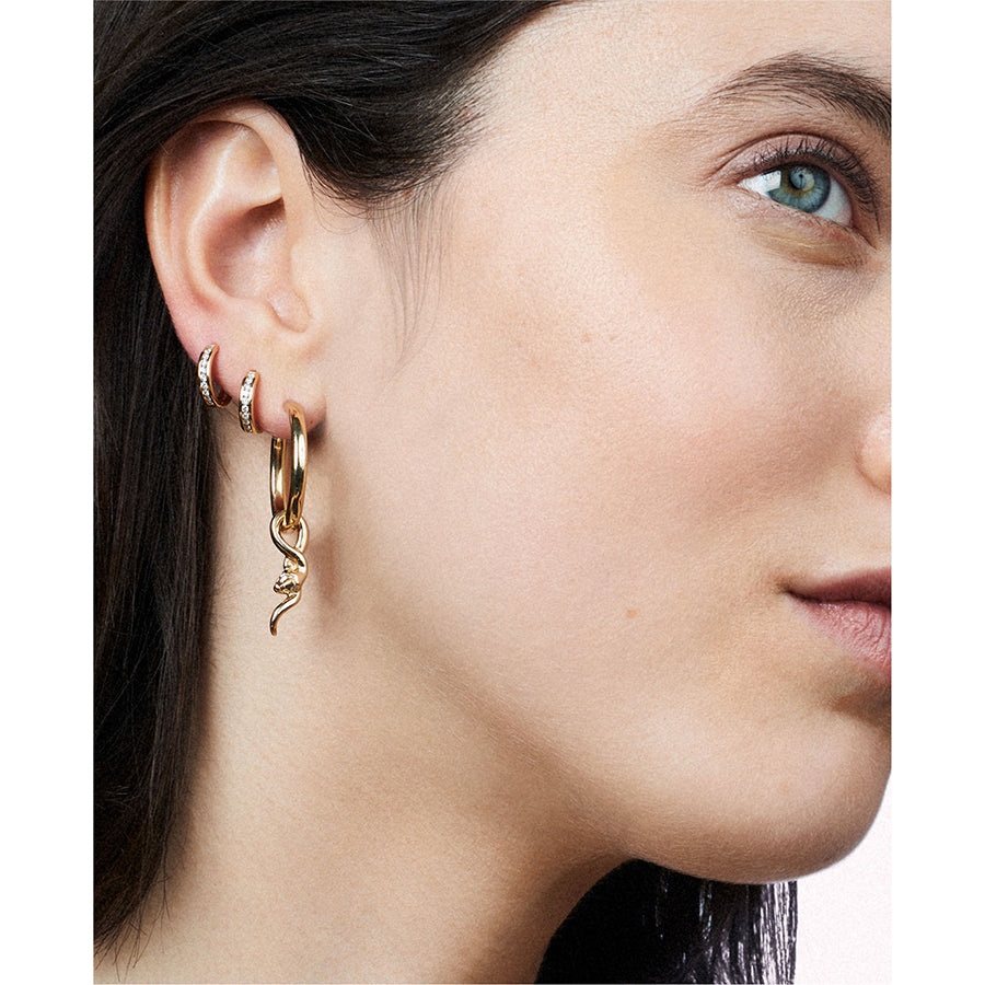 A light complexion model wearing three earrings on her ear. Two yellow gold hoops with a line of white diamonds and one hoop with a serpent charm hanging from it.