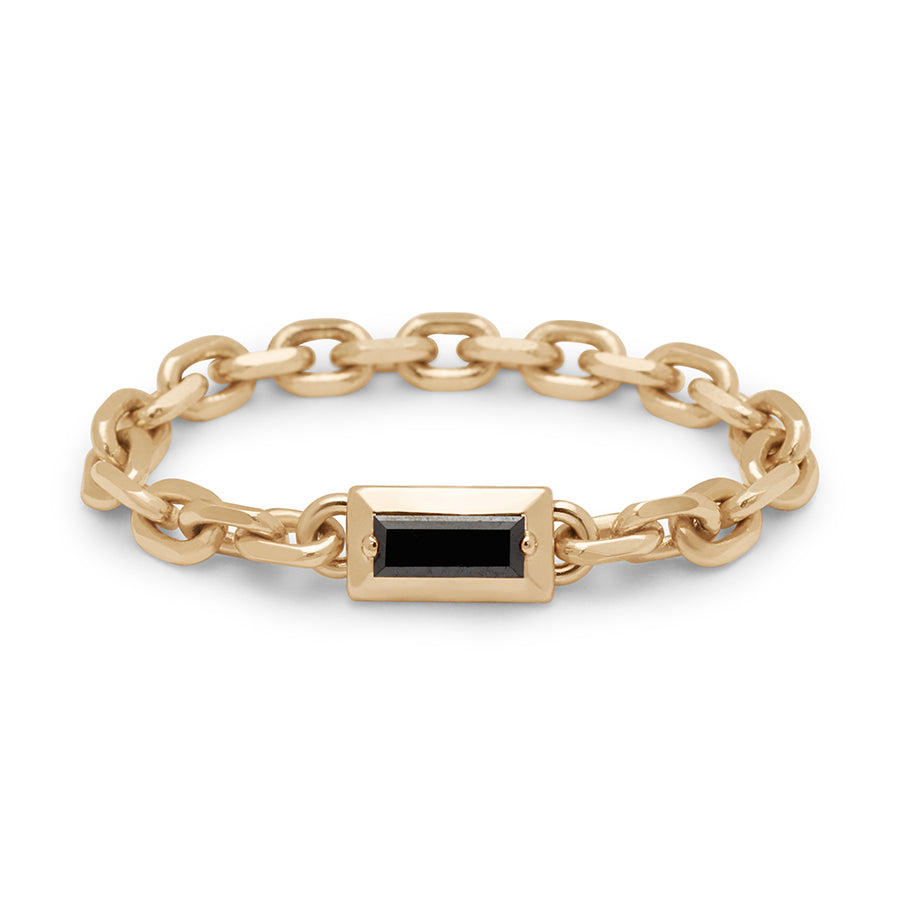 A band with a bezel set black diamond baguette in a yellow gold chain setting.