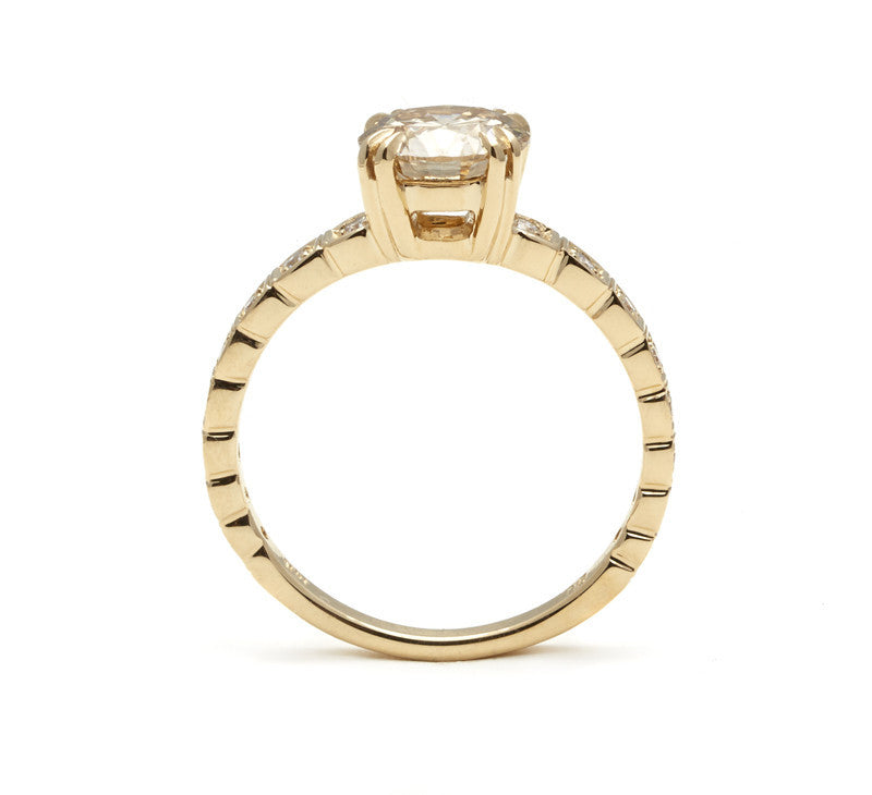 Side view of a solitaire ring with a brilliant cut champagne diamond with white diamond pave around the band set in yellow gold.