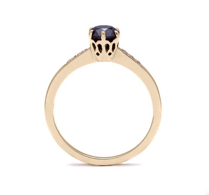 Side view of a solitaire ring with a round black diamond with white diamond pave on either side set in yellow gold.