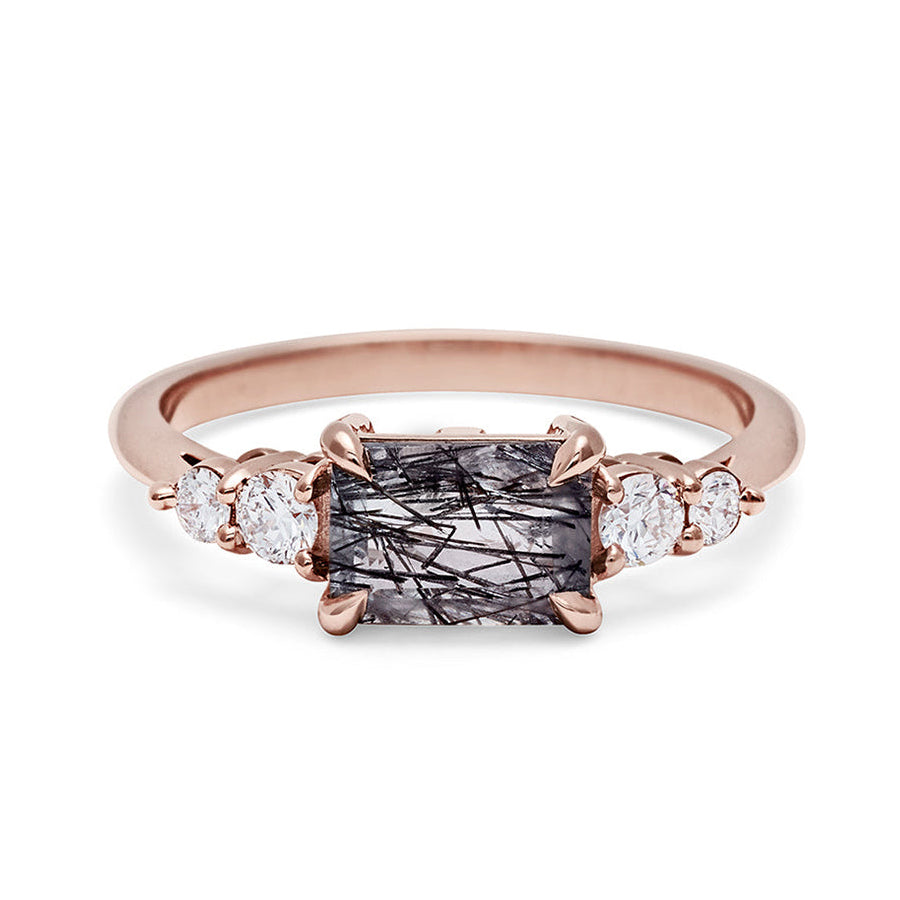 A ring with an emerald shaped black rutilated quartz center stone with two round white diamonds on either side set in rose gold., Rose Gold