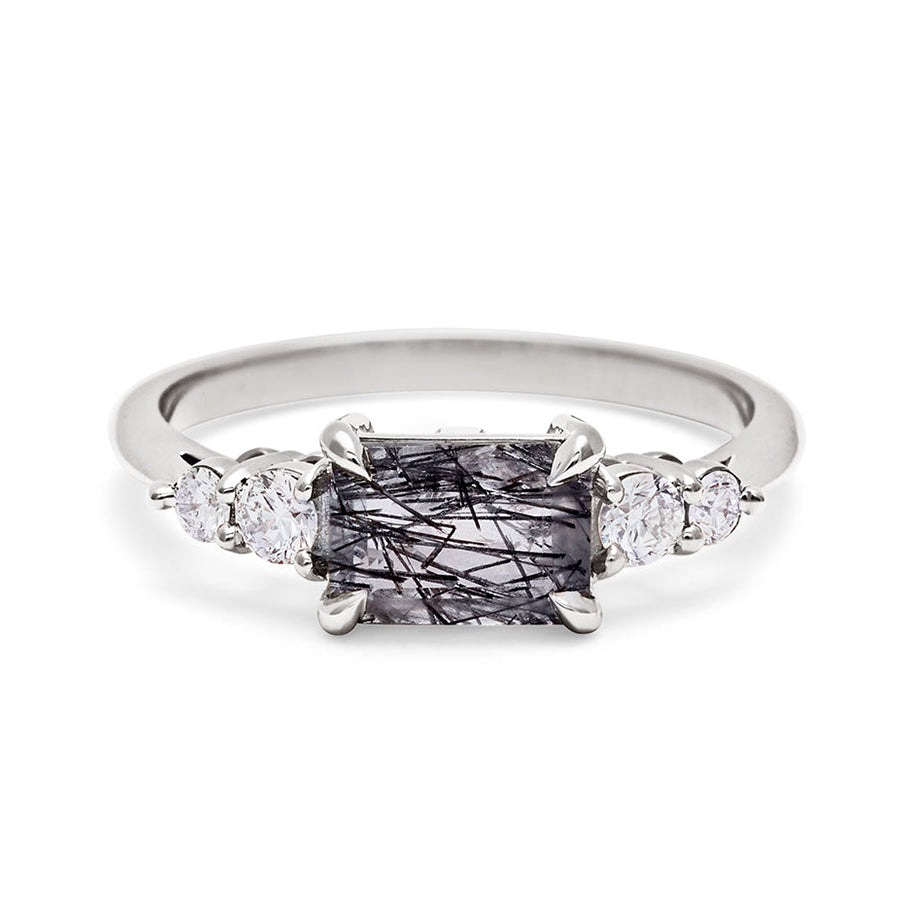 A ring with an emerald shaped black rutilated quartz center stone with two round white diamonds on either side set in white gold., White Gold