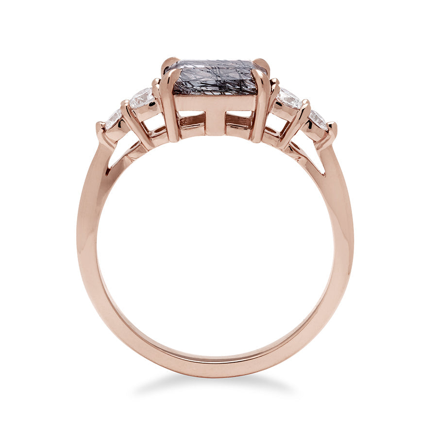 Side view of a ring with an emerald shaped black rutilated quartz center stone with two round white diamonds on either side set in rose gold., Rose Gold