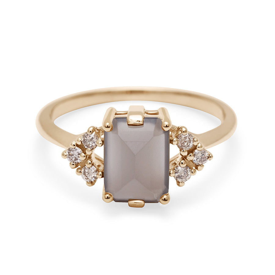 A ring with an emerald cut grey moonstone center with three round champagne diamonds on either side in arrow shape, set in yellow gold.