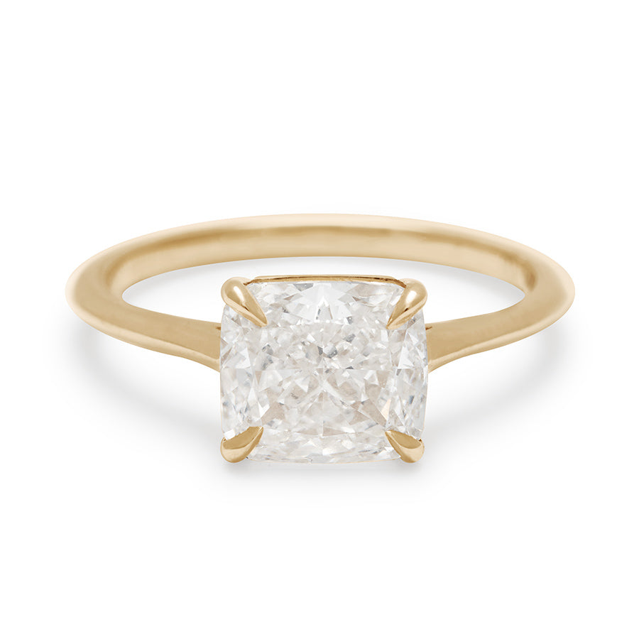 An east/west solitaire ring with a cushion cut white diamond stone set in yellow gold.