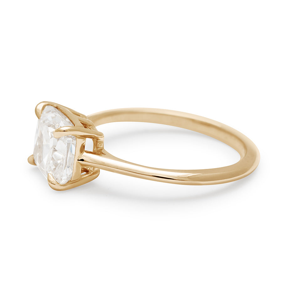 Angled view of an east/west solitaire ring with a cushion cut white diamond stone set in yellow gold.