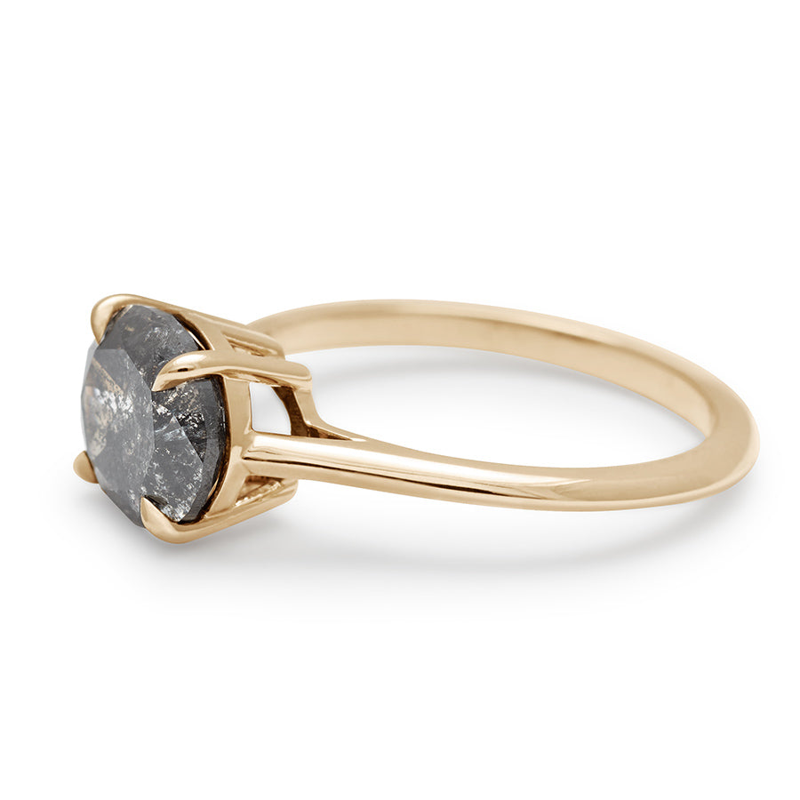 Angled view of an east/west solitaire ring with an oval shape grey diamond stone set in yellow gold.