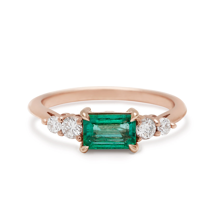 A ring with an emerald cut and shaped green emerald center stone with two round white diamonds on either side set in rose gold., Rose Gold