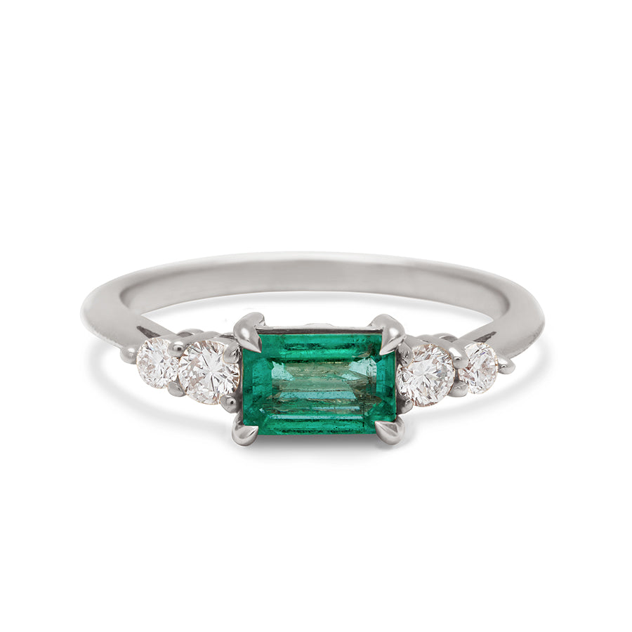 A ring with an emerald cut and shaped green emerald center stone with two round white diamonds on either side set in white gold., White Gold