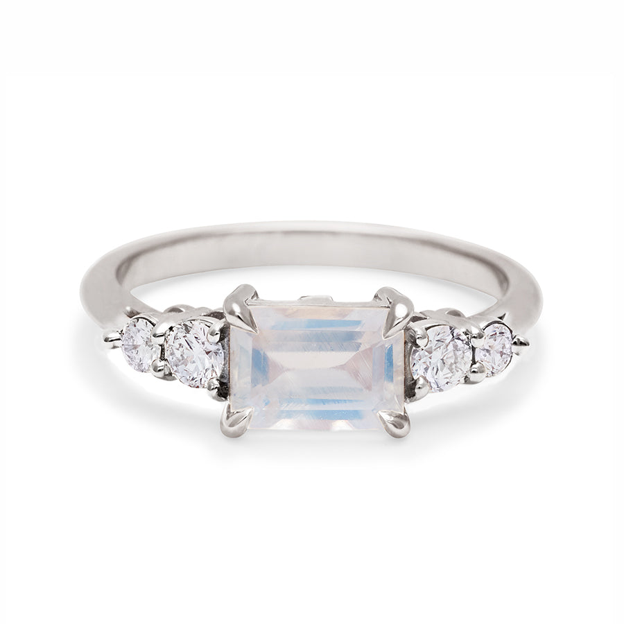 A ring with an emerald cut and shaped rainbow moonstone center stone with two round white diamonds on either side set in white gold., White Gold