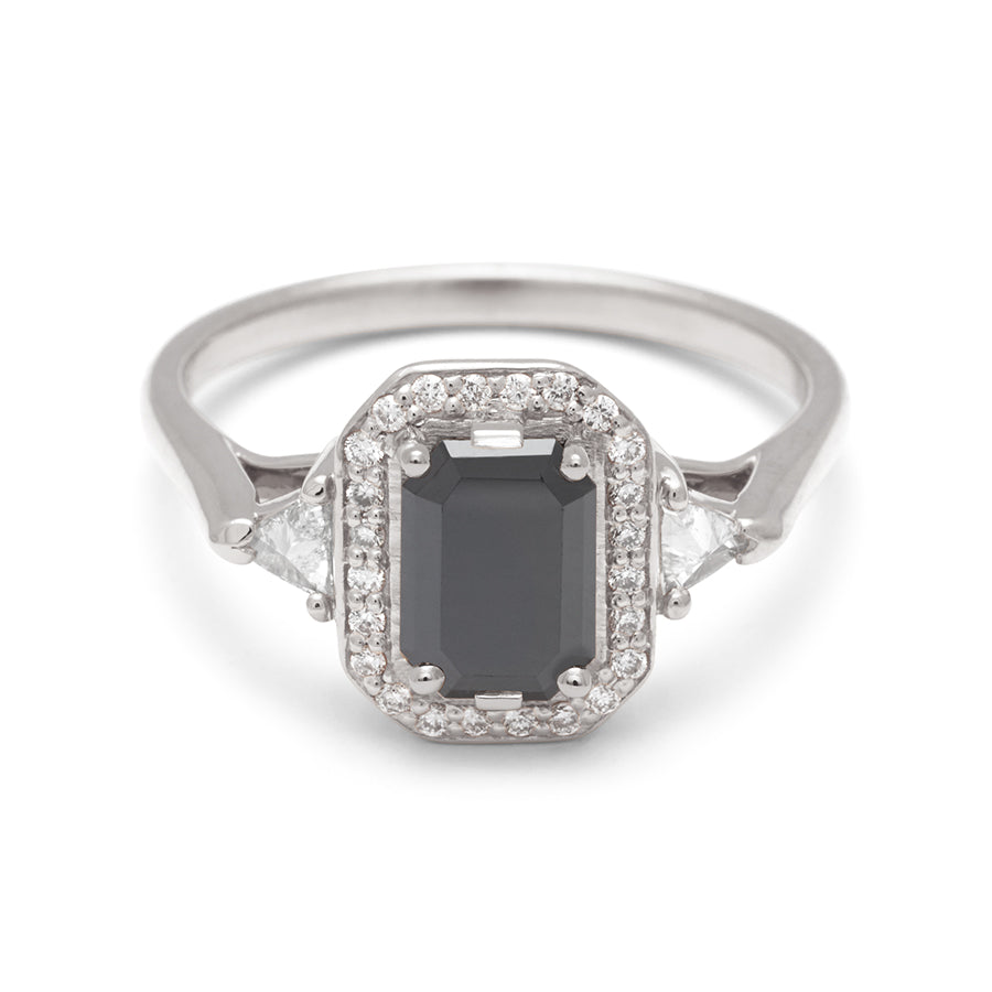 A three stone engagement ring with an emerald cut and emerald shape black diamond center stone surrounded by a white diamond pave halo with two white diamond trillion side stones set in white gold., White Gold