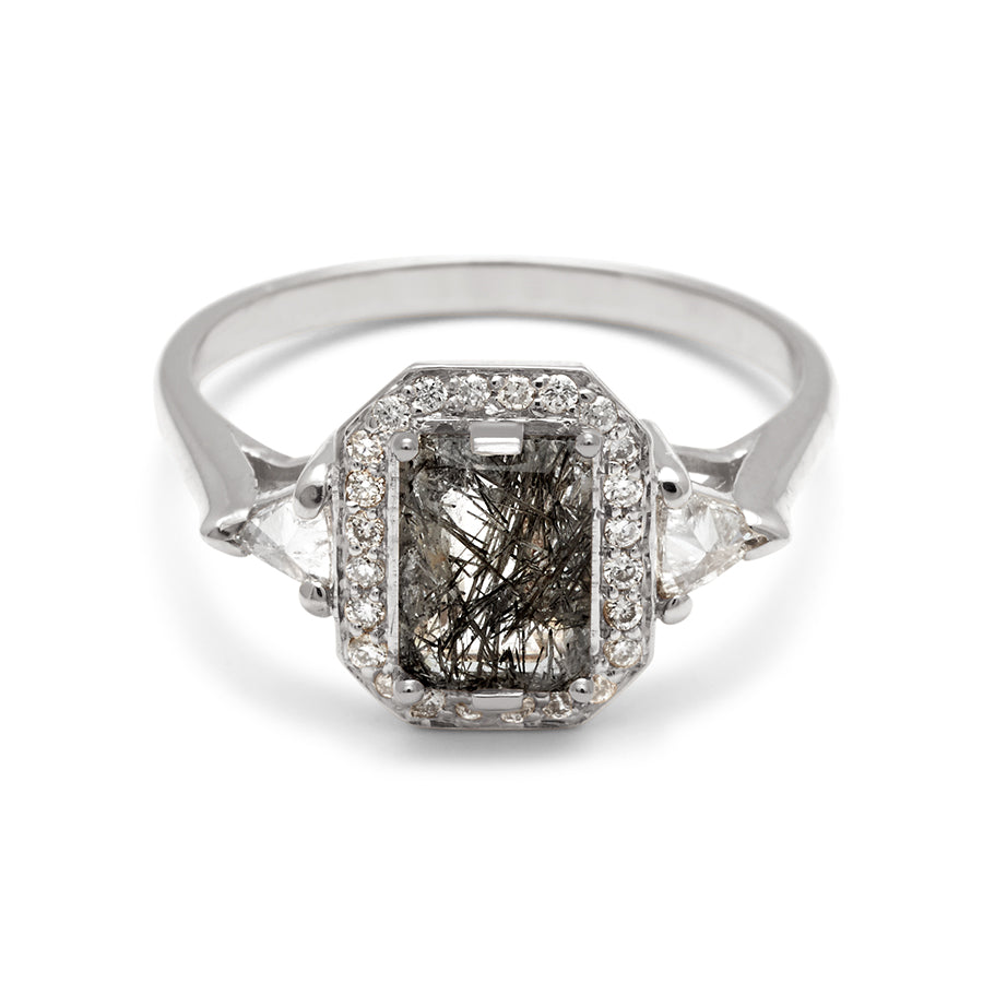 A three stone engagement ring with an emerald cut and emerald shape black rutilated quartz center stone surrounded by a white diamond pave halo with two white diamond trillion side stones set in white gold., White Gold
