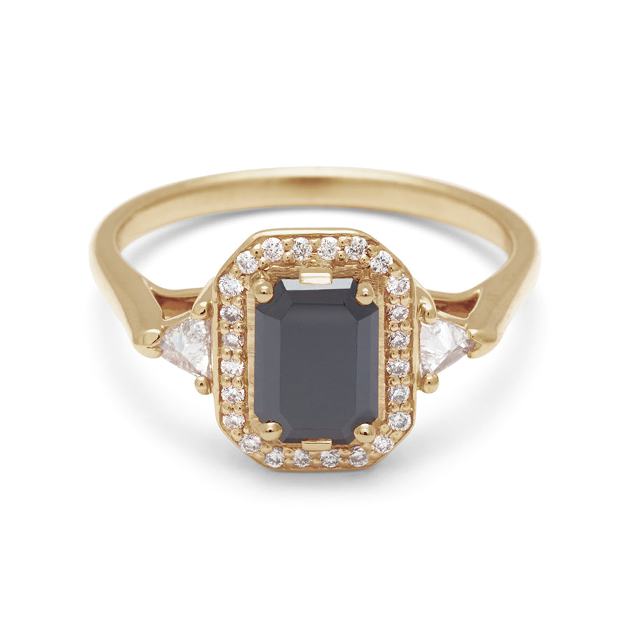 A three stone engagement ring with an emerald cut and emerald shape black diamond center stone surrounded by a white diamond pave halo with two white diamond trillion side stones set in yellow gold., Yellow Gold