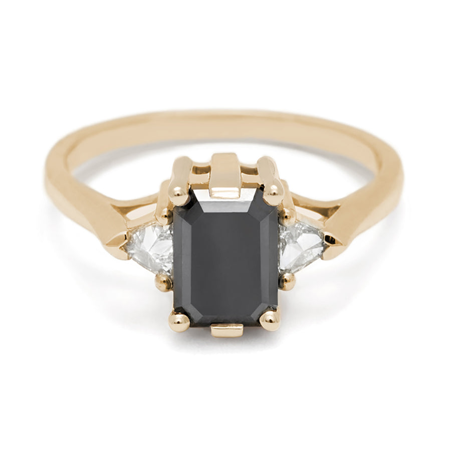 A three stone engagement ring with an emerald cut and emerald shape 7x5mm black diamond center stone with two white diamond trillion side stones set in yellow gold., Yellow Gold