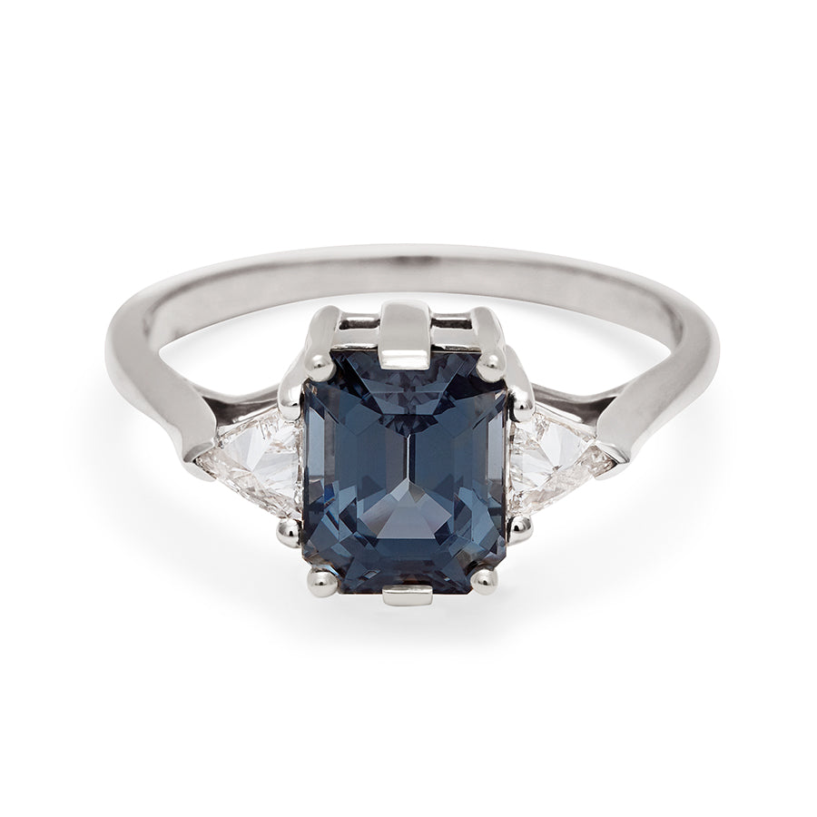 A three stone engagement ring with an emerald cut and emerald shape grey spinel center stone with two white diamond trillion side stones set in white gold., White Gold