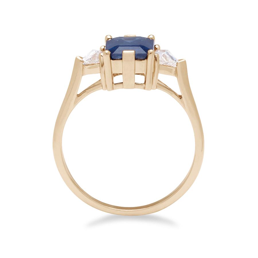 Side view of a three stone engagement ring with an emerald cut and emerald shape blue sapphire center stone with two white diamond trillion side stones set in yellow gold.