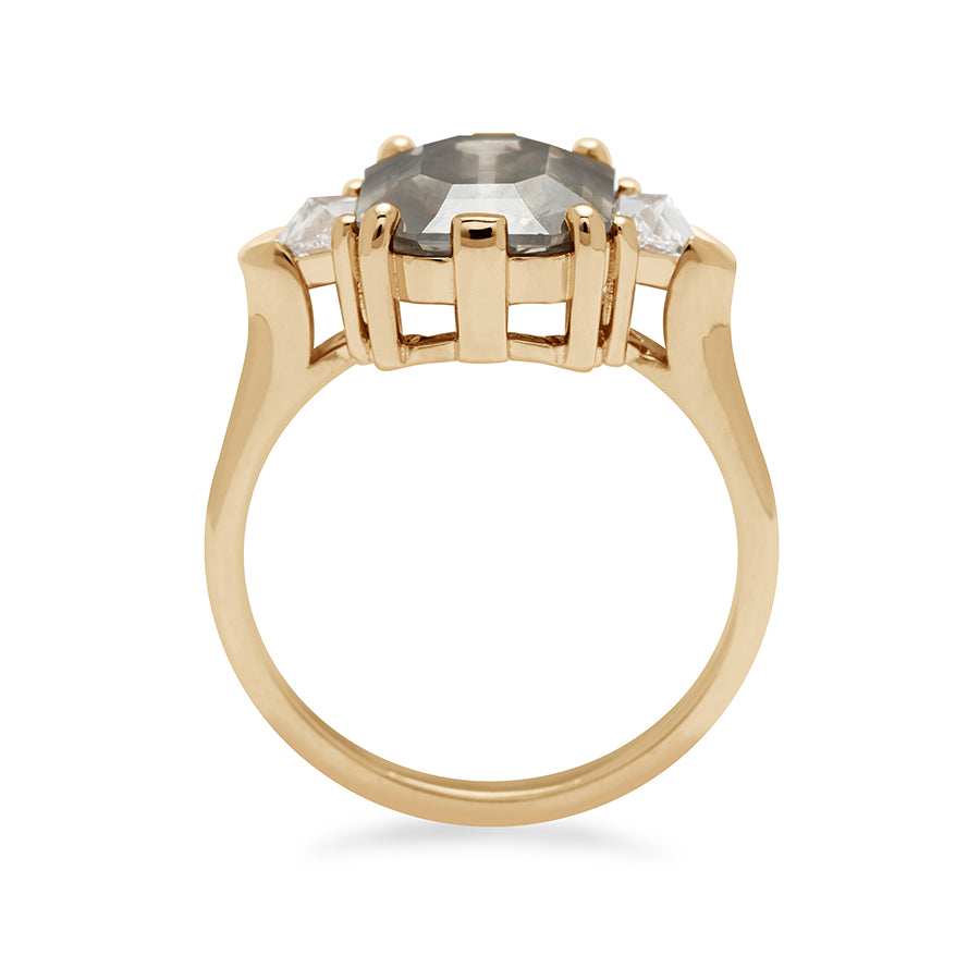 Side view of a three stone engagement ring with an emerald cut and emerald shape grey diamond center stone with two white diamond trillion side stones set in yellow gold.