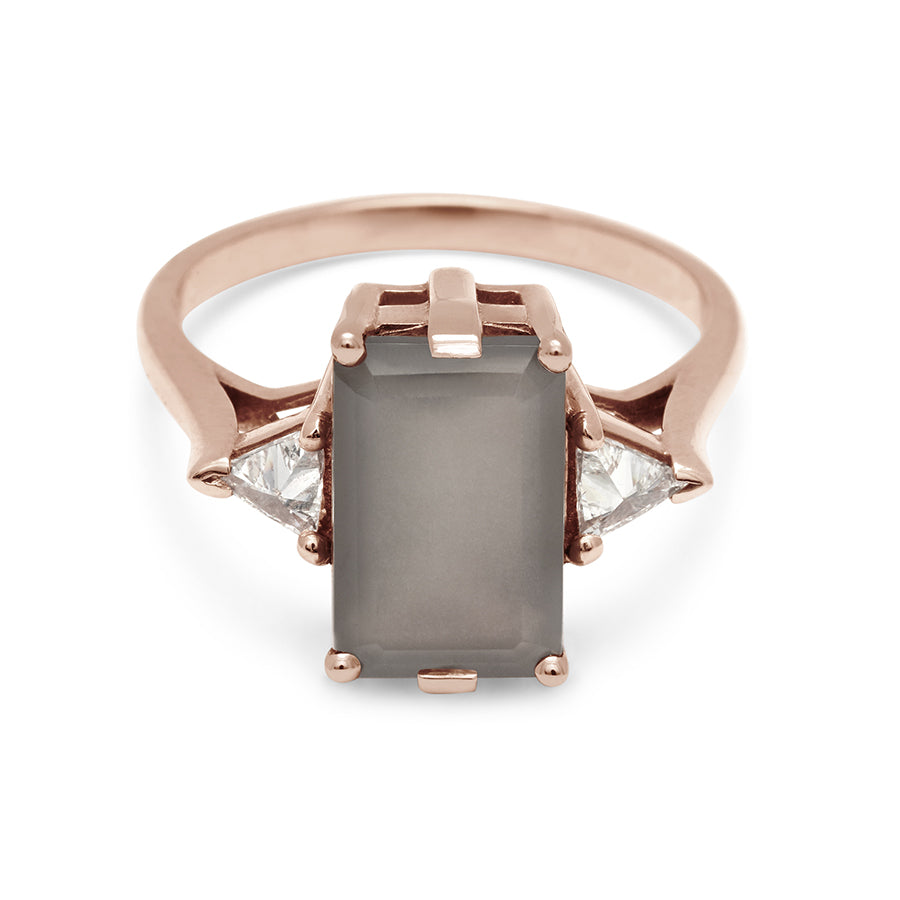 A three stone engagement ring with an emerald shape grey moonstone center stone with two white diamond trillion side stones set in rose gold., Rose Gold