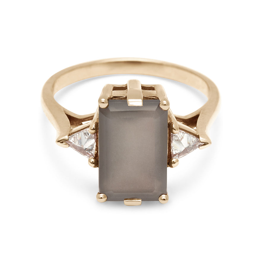 A three stone engagement ring with an emerald shape grey moonstone center stone with two white diamond trillion side stones set in yellow gold., Yellow Gold