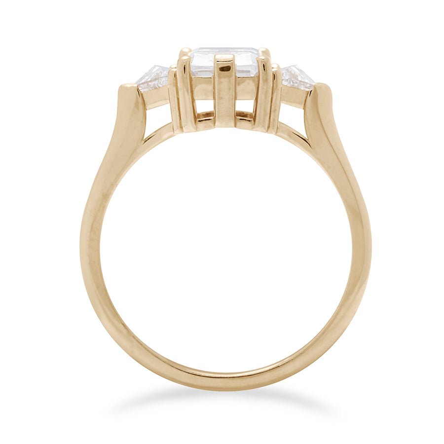 Side view of a three stone engagement ring with a 8x6mm emerald cut and emerald shape white diamond center stone with two white diamond trillion side stones set in yellow gold., Yellow Gold