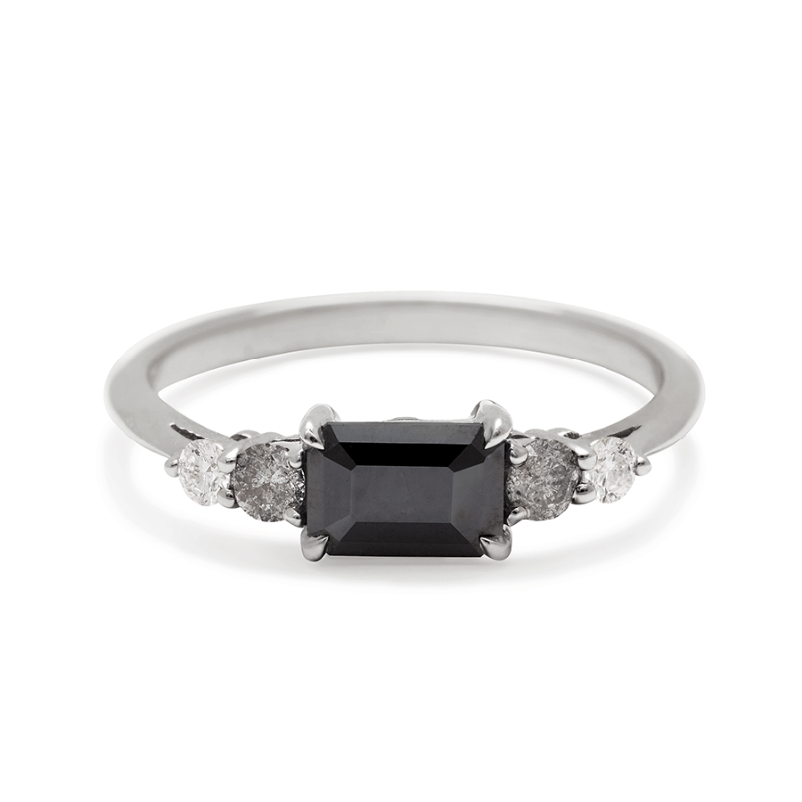 A ring with an emerald cut and shaped black diamond center stone with one round white diamond and one round grey diamond on either side set in white gold., White Gold