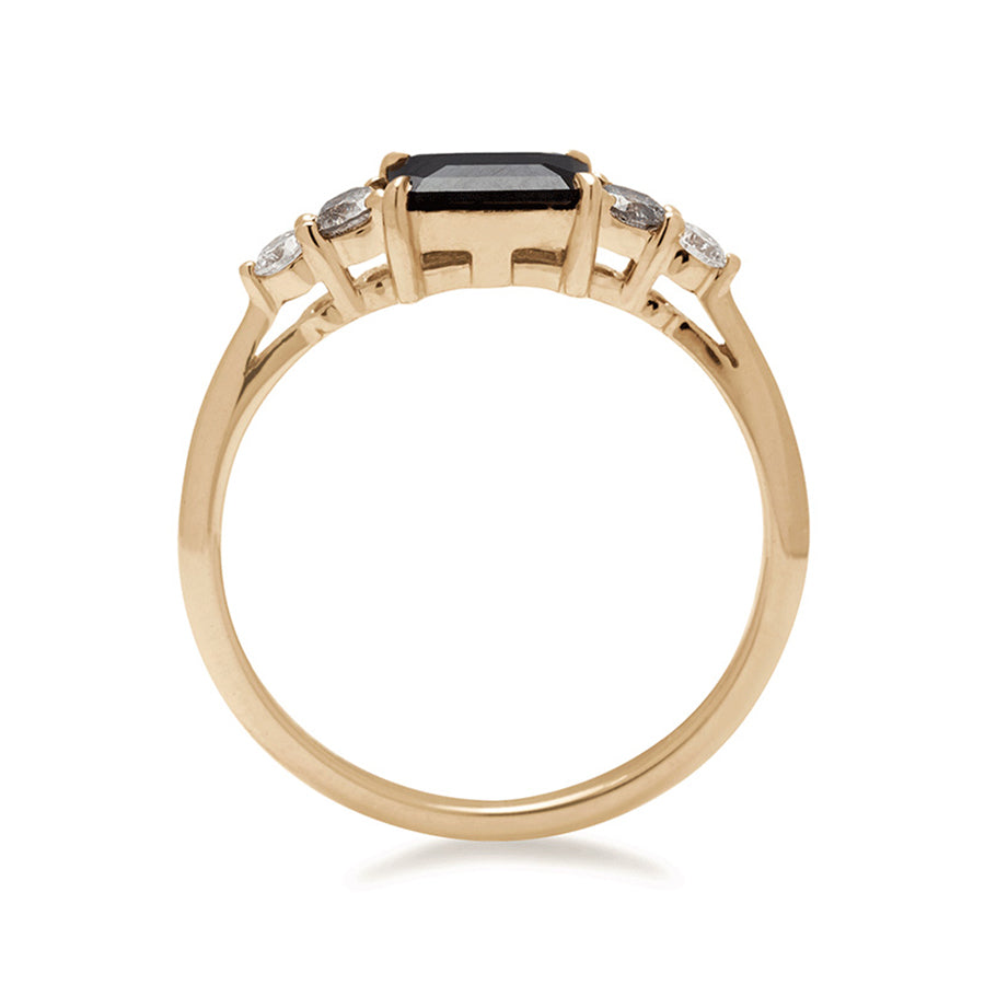 A side view of a ring with an emerald cut and shaped black diamond center stone with one round white diamond and one round grey diamond on either side set in yellow gold.,Yellow Gold